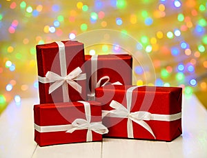 Red gift boxes with ribbon against golden bokeh background, free space. Holiday greeting card for birthday, wedding.