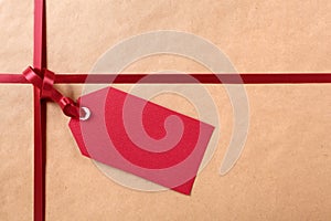 Red gift tag and ribbon, brown wrapping paper background