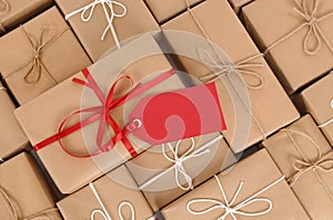 Red gift tag with rows of brown paper packages in background, copy space