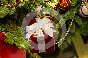 Red giftbox with ribbon and bow, small box on the background of the Christmas tree