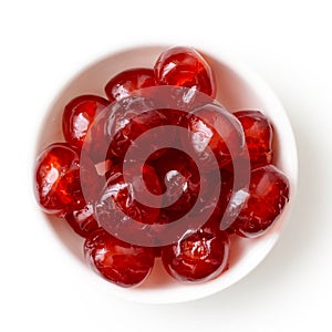 Red glace cherries in white bowl isolated on white from above.