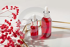 Red glass bottles with dropper pipette with serum or essential oil on glass plate for product presentation.