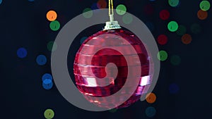 Red glass Christmas ornament rotating with blinking lights behind