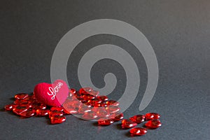 Red glass hearts and a soft plush heart with the words Love on a black background - Valentine`s day. Holiday, banner, copyspace.