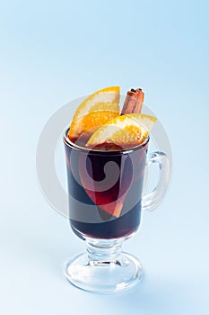 Red glogg or mulled wine with orange slices and cinnamon stick on blue background, vertical