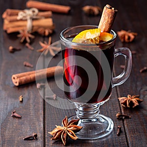 Red glogg or mulled wine with orange slices and cinnamon stick on dark wooden background, square format photo