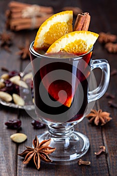 Red glogg or mulled wine with orange slices and cinnamon stick on dark wooden background, vertical, closeup