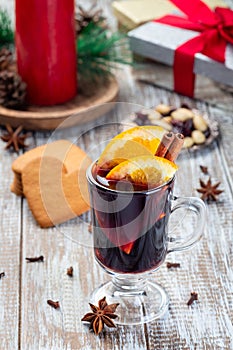 Red glogg or mulled wine with orange slices and cinnamon stick, gingerbread cookies and gift box on  background, vertical