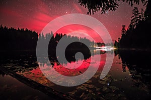 Red glowing sky at night with stars milky way and shooting star at big Arbersee in bavarian forest, Germany