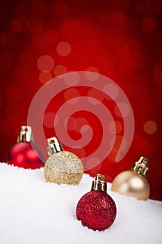 Red and gold Christmas baubles on snow, red background