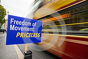 Red and gold London bus with motion blur as it passes anti-Brexit Freedom of Movement sign