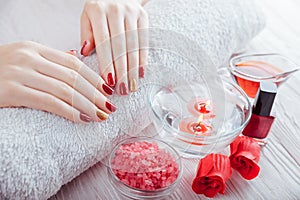 Red and golden manicure with spa essentials on white wooden table.