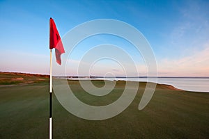 Red golf flag on a green at dawn