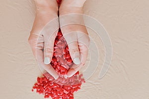 Red granules of depilatory wax are scattered in handfuls in the hands of a girl with a white manicure. a handful of granule wax in