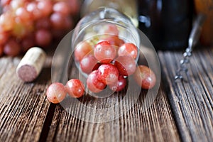 Red grapes, glass, bottle of red wine, cork and corkscrew on vintage wooden background. Close-up, selective focus, shallow depth