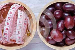 Red grapes and tape measure in wooden bowl.