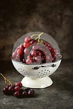 Red grapes in a white colander on a gray background.