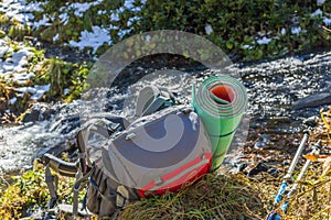 Red-gray rucksack and trekking poles at river background