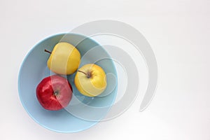 Red and green apple on blue plate. Overhead view of fresh fruits and striped gray cloth napkin on white table background.