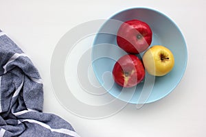 Red and green apple on blue plate. Overhead view of fresh fruits and striped gray cloth napkin on white table background.