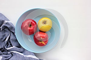 Red and green apple on blue plate. Overhead view of fresh fruits and striped gray cloth napkin on white table background.