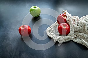 Red and green apples in cotton mesh eco bag on a dark background