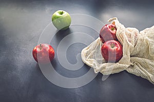 Red and green apples in cotton mesh eco bag on a dark background