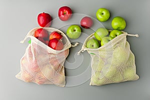 Red and green apples in mesh grocery bags on a gray background, flat lay.