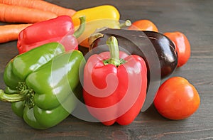 Red and green bell peppers with other colorful vegetables on dark brown wooden background