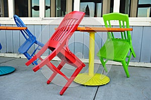 Red, Green, and Blue Chairs Leaning on Tables