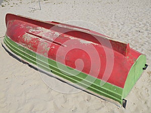 Red and green boat rotated up side down to sand