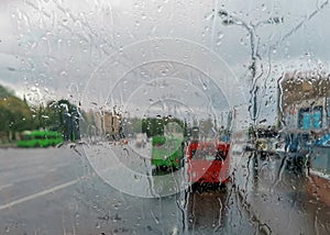 Red and green buses on a city street through a cloudy windshield in rain drops during a downpour