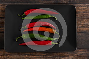 Red and green chili peppers on a black plate on a wooden table. Top view