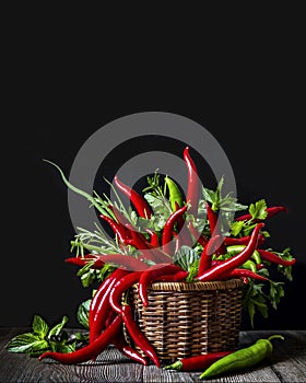 Red and green chili peppers with fresh herbs in a wicker basket on a wooden table