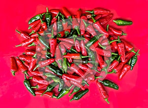 Red and green chilli peppers. Heap on red background.