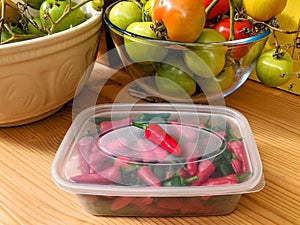 Red and green chilli peppers in plastic kitchen container.
