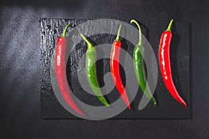 Red and green chillies on blackboard base on black background. Top view. Gastronomy and cooking condiments