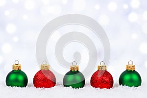 Red and green Christmas ornaments in snow with twinkling background