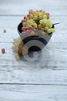 Red green grapes in a black bowl on a gray wooden table