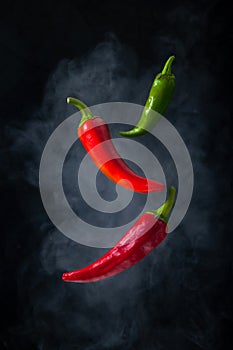 Red and Green Hot Chili Peppers Levitation in the Air with Smoke on Black Background