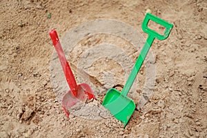 Red and green kids toddlers plastic play shovels laying on a sandbox sand background