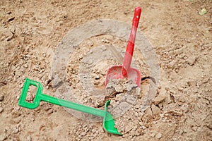 Red and green kids toddlers plastic play shovels laying on a sandbox sand background