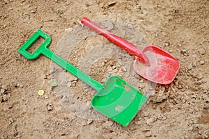 Red and green kids toddlers plastic play shovels laying on a sandbox sand background