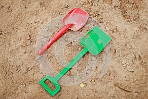 Red and green kids toddlers plastic play shovels laying on a sandbox sand background