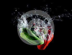 Red and green paprika falling in water on black background