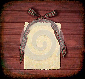 Red and Green plaid Christmas Bow with Paper with ragged edges on Brown Rustic Wood Boards Background with copy space. The tones a