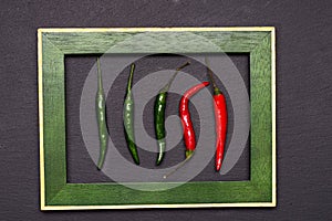 Red and green: a tangy pair of fresh chili pods against a black background in a portrait frame. Table top view, flat lay, copy