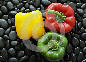 Red, green and yellow bell peppers on black stone that has smooth glossy skin and round edge.