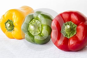 Red and green and yellow bell peppers in a row on white background.