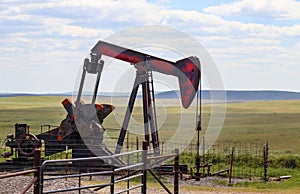 Red and grey and orange pumpjack on oil well in the plains with cattle grazing behind